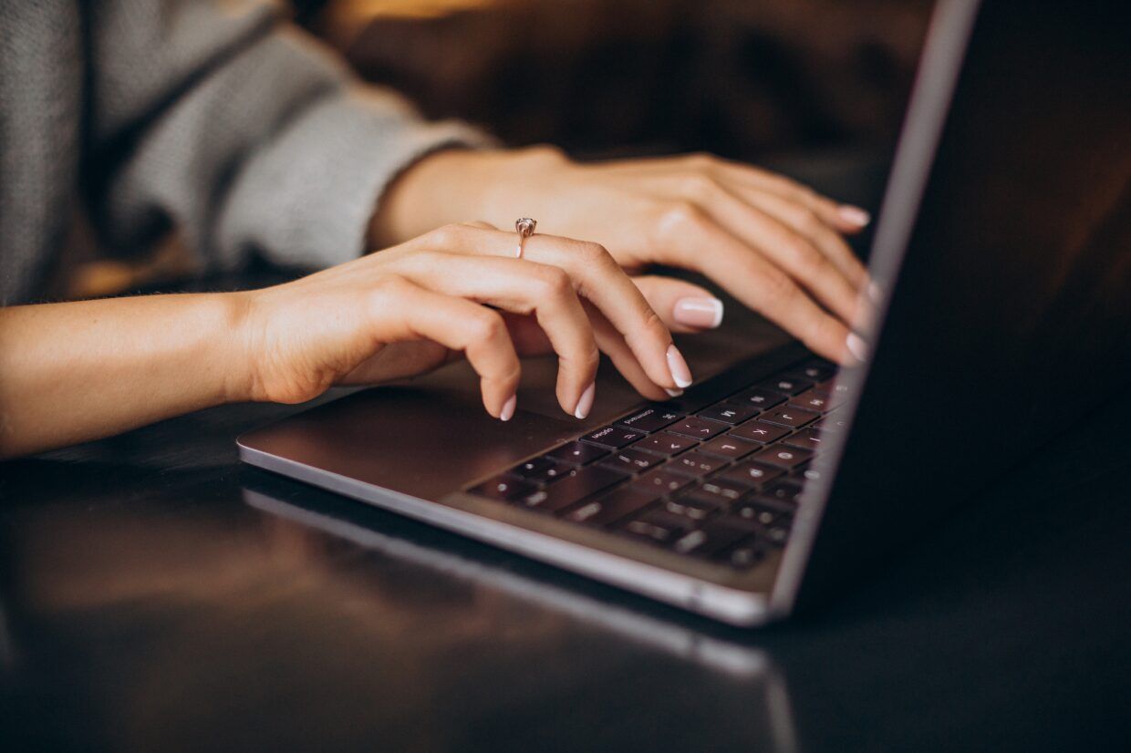 Laptop billentyűzetén gépelő kéz közelről, sötét asztallapon