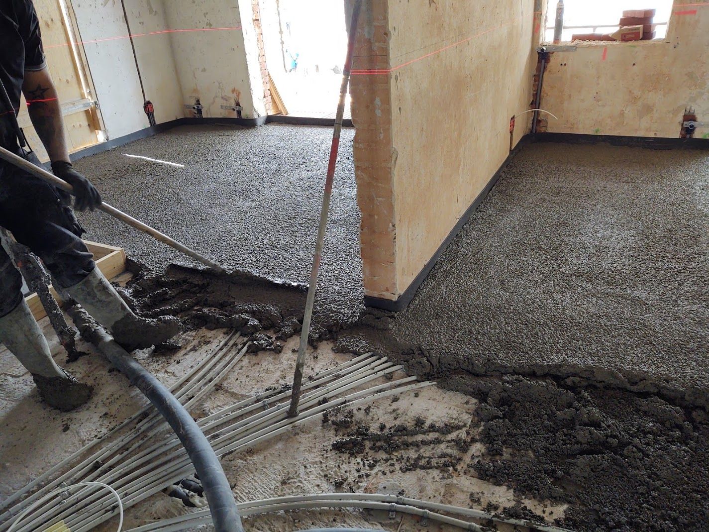 Thermobeton aljzat bedolgozása egy épülő lakás padlóján, a gépészeti vezetékek fölött